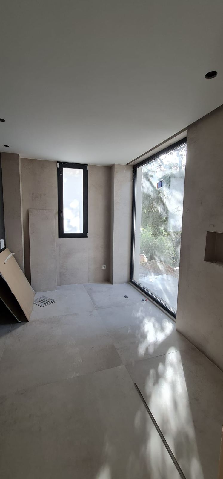 Baño amplio con ventanal y ventana vertical, techo continuo sin elementos de climatización visibles.
