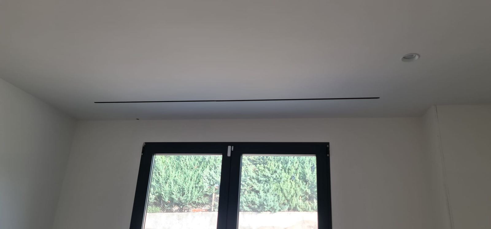 Dormitorio con difusor lineal de ranura en el techo, sobre la ventana.