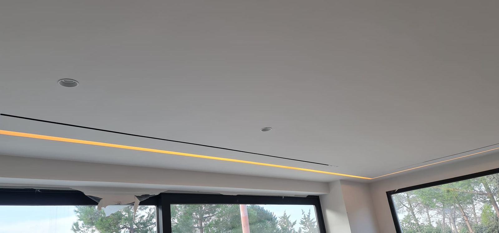 Difusor lineal negro en el techo, paralelo a la tira de luz LED cálida que recorre el perímetro.