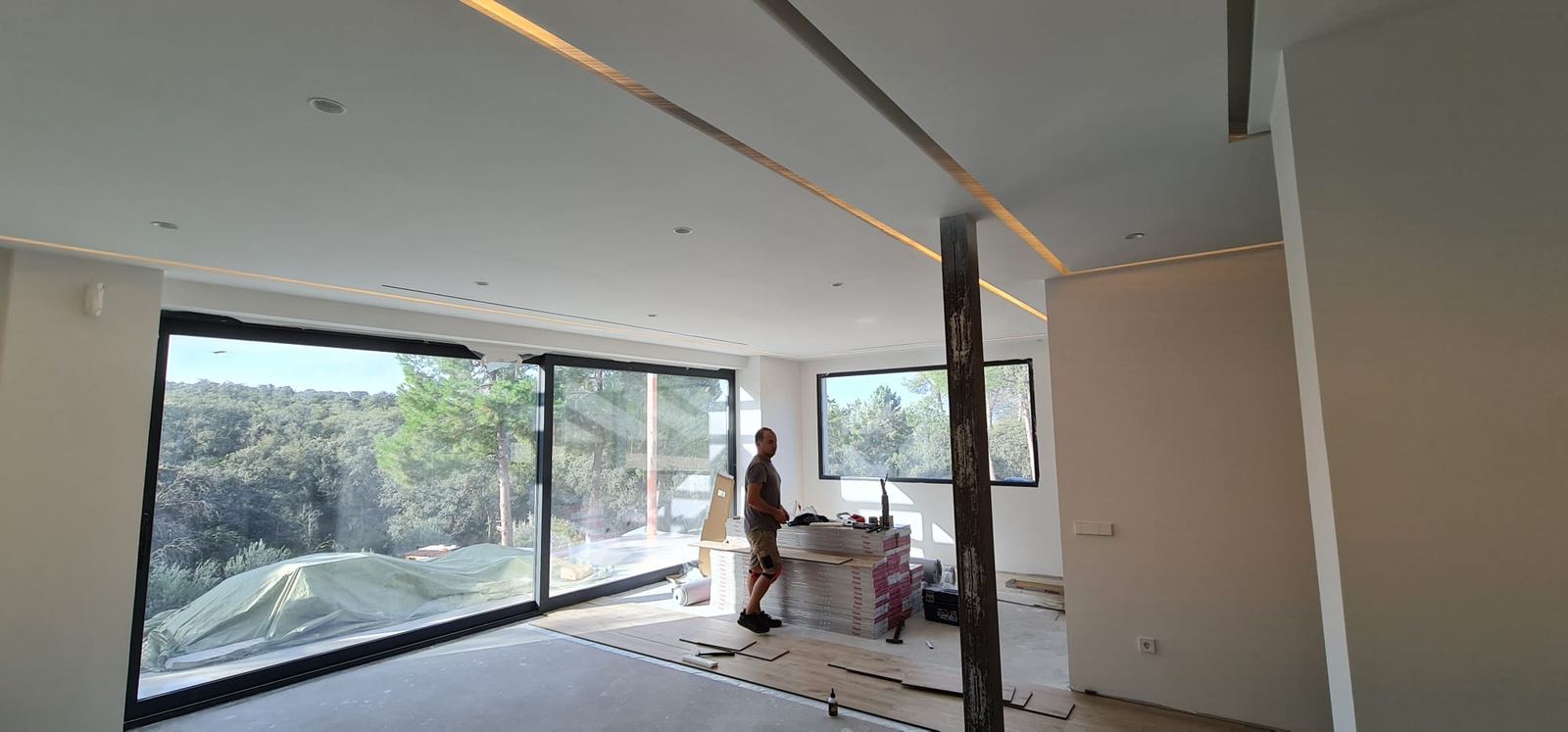 Salón diáfano con grandes ventanales: difusor lineal en el techo junto a una línea de luz LED indirecta.