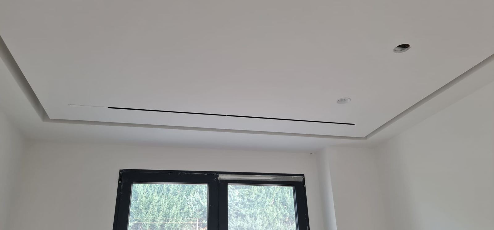 Techo con bandeja rebajada y difusor lineal integrado en el borde, sobre la ventana del dormitorio.